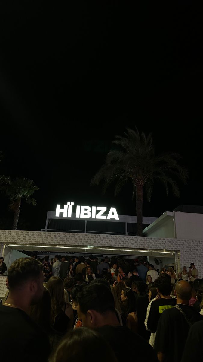 a crowd of people standing in front of a building with a sign that reads hibiza