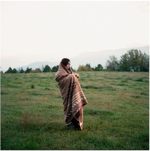 a woman wrapped in a blanket standing on top of a lush green field