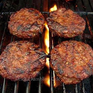 four hamburger patties cooking on the grill