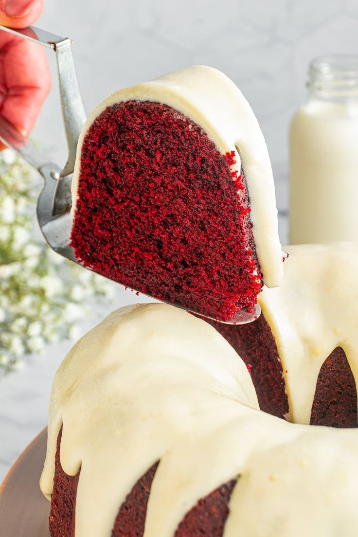 someone is cutting into a red velvet bundt cake with white icing on it