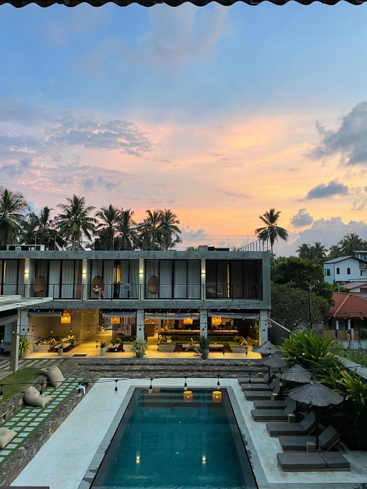 an outdoor swimming pool with lounge chairs and umbrellas in front of the house at sunset