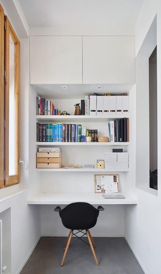 a chair sitting in front of a white desk with books on the shelves and an open window