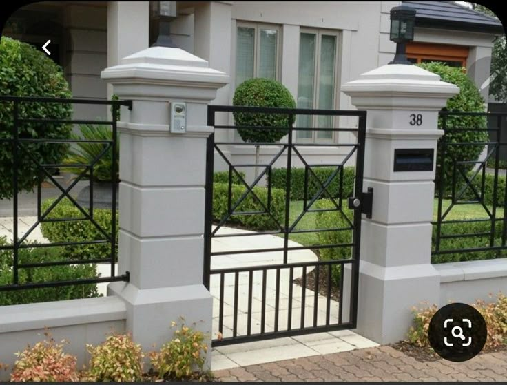 an iron gate is shown in front of a house with bushes and shrubs around it