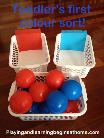 two plastic baskets filled with balloons on top of a wooden floor next to a sign that says toddler's first color sort