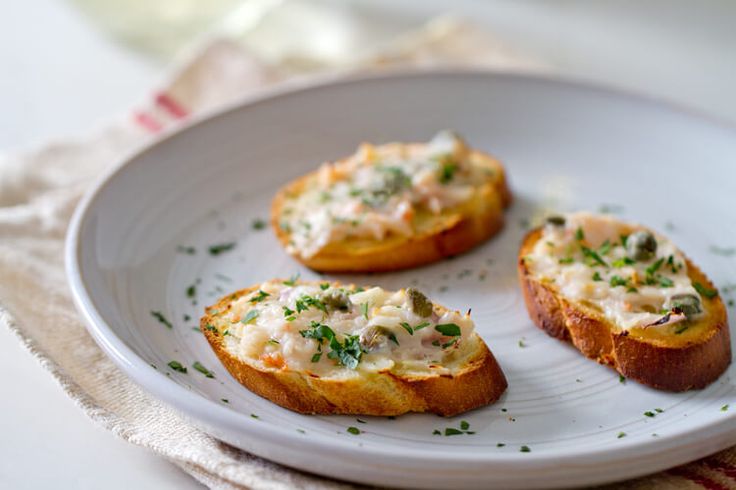 three pieces of bread with cheese and herbs on it sitting on a plate next to a napkin