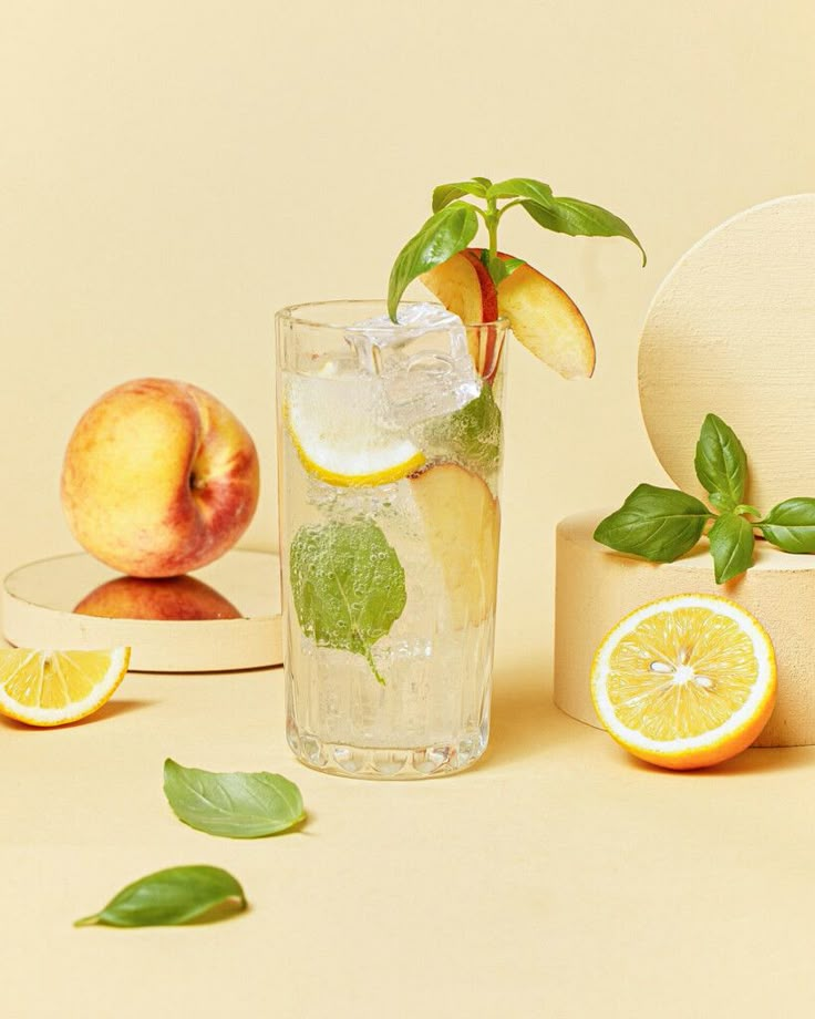 a glass with ice and lemon slices next to some sliced peaches on a table