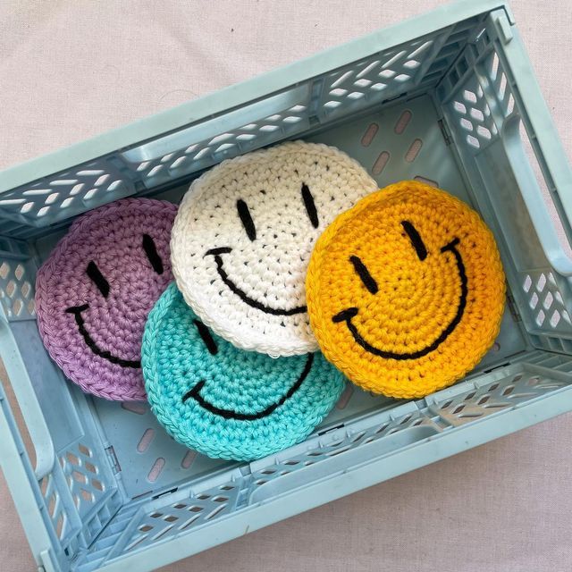 three crocheted smiley faces sitting on top of each other in a blue basket