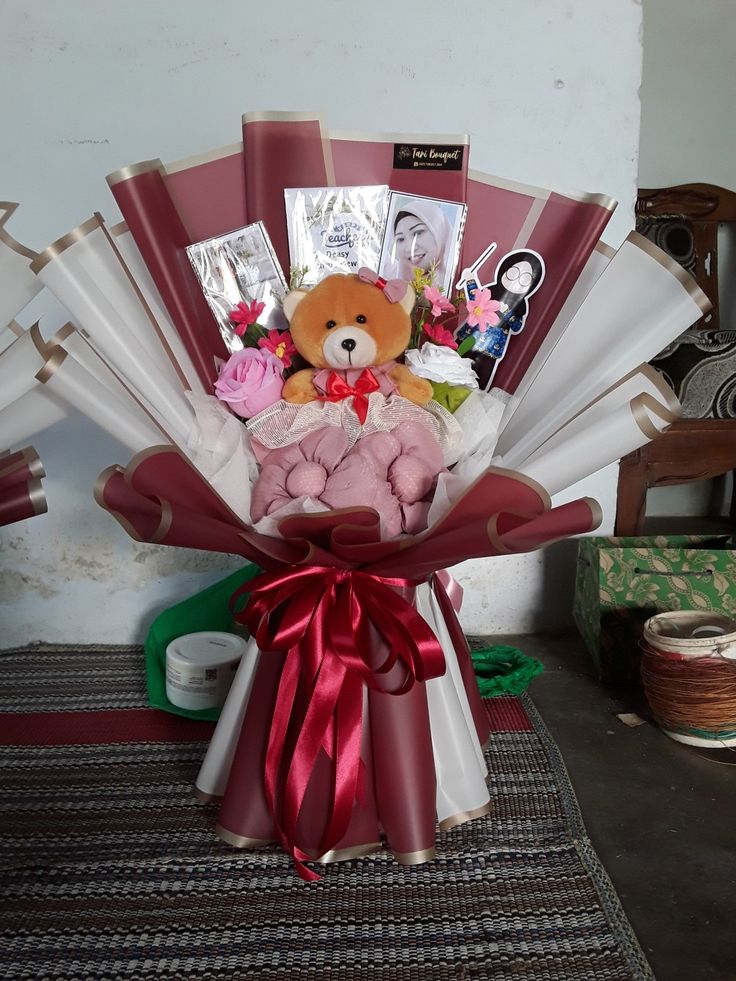 a teddy bear sitting on top of a bunch of wrapped paper in a vase filled with flowers