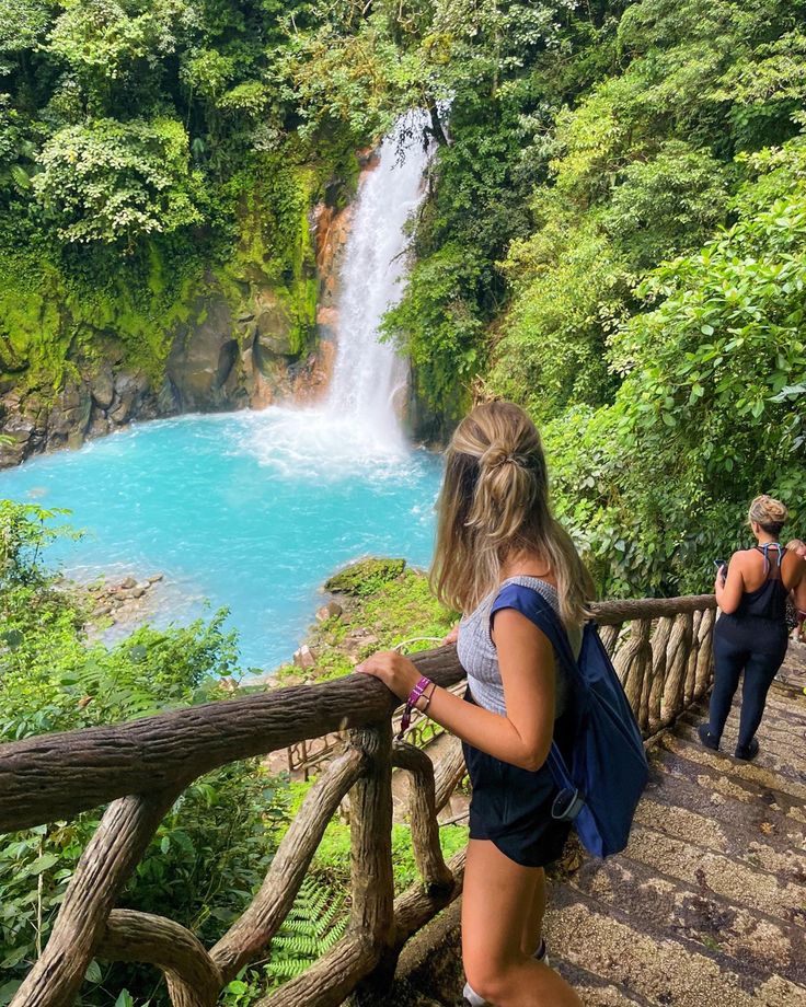 two people standing at the top of stairs looking down at a waterfall and blue water