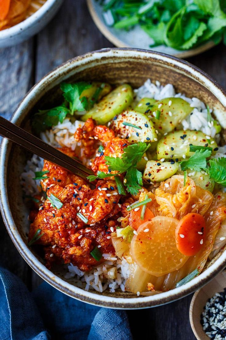 a bowl filled with rice, vegetables and meat on top of a wooden table next to other bowls