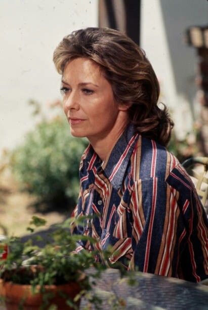 a woman sitting at a table with potted plants in front of her and looking off into the distance