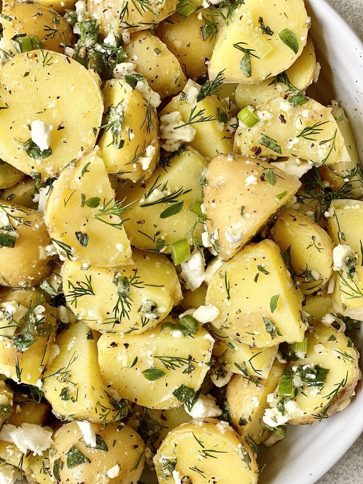 a white bowl filled with potatoes covered in feta cheese and dill sprigs