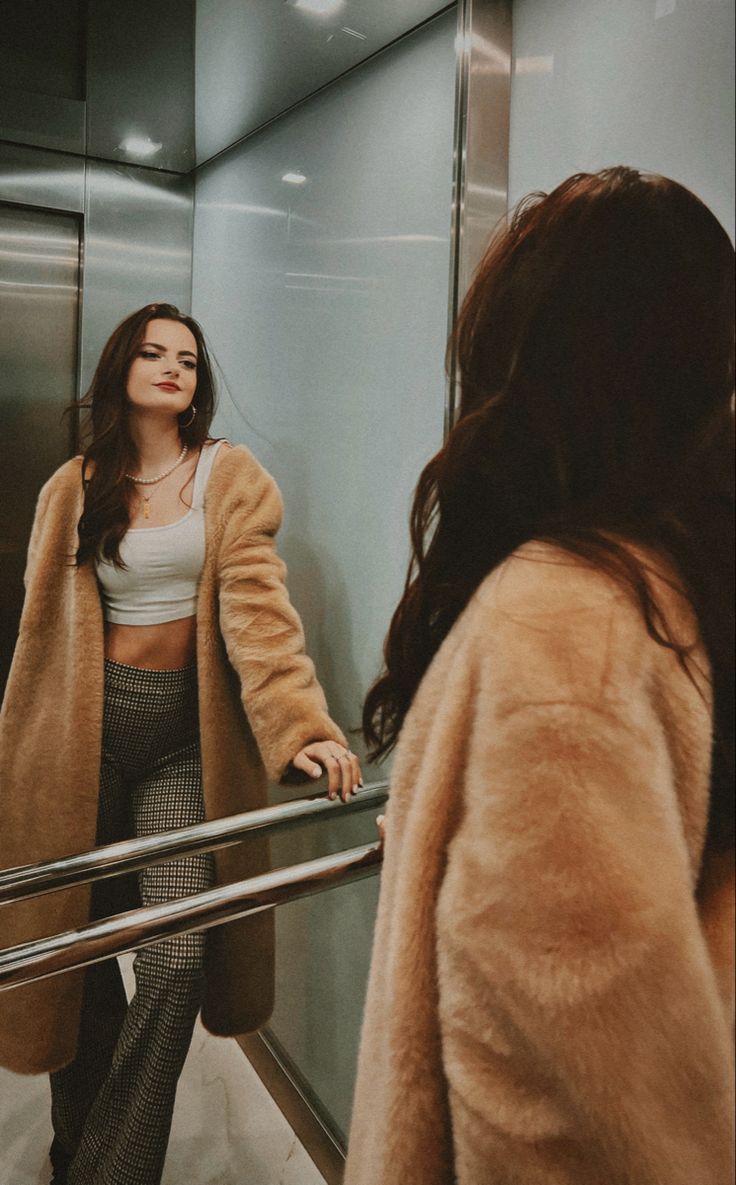 a woman is standing on an escalator and looking at herself in the mirror