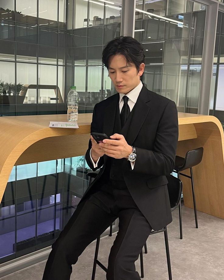 a man in a suit sitting on a chair looking at his cell phone