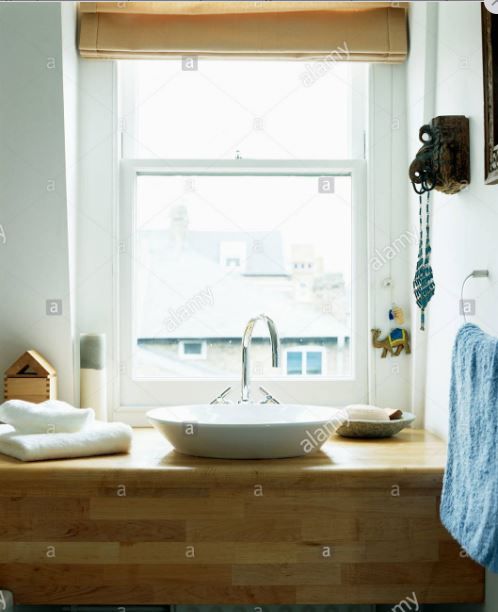 a bathroom sink sitting under a window in front of a window sill with towels on it