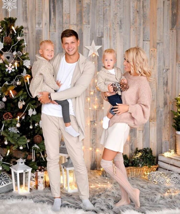 a man and woman holding two children in front of a christmas tree with lights on it