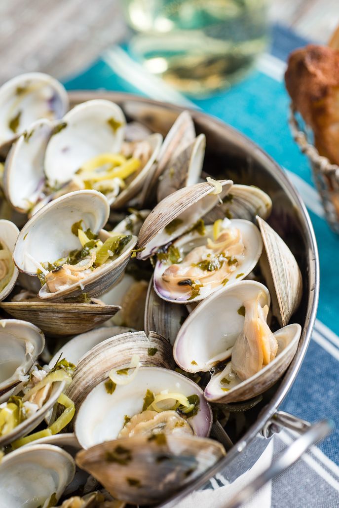 a pan filled with lots of clams on top of a blue table cloth next to bread