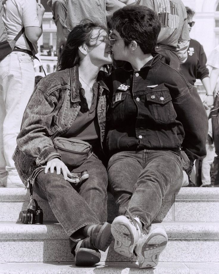 black and white photograph of two people sitting on steps kissing each other with others in the background