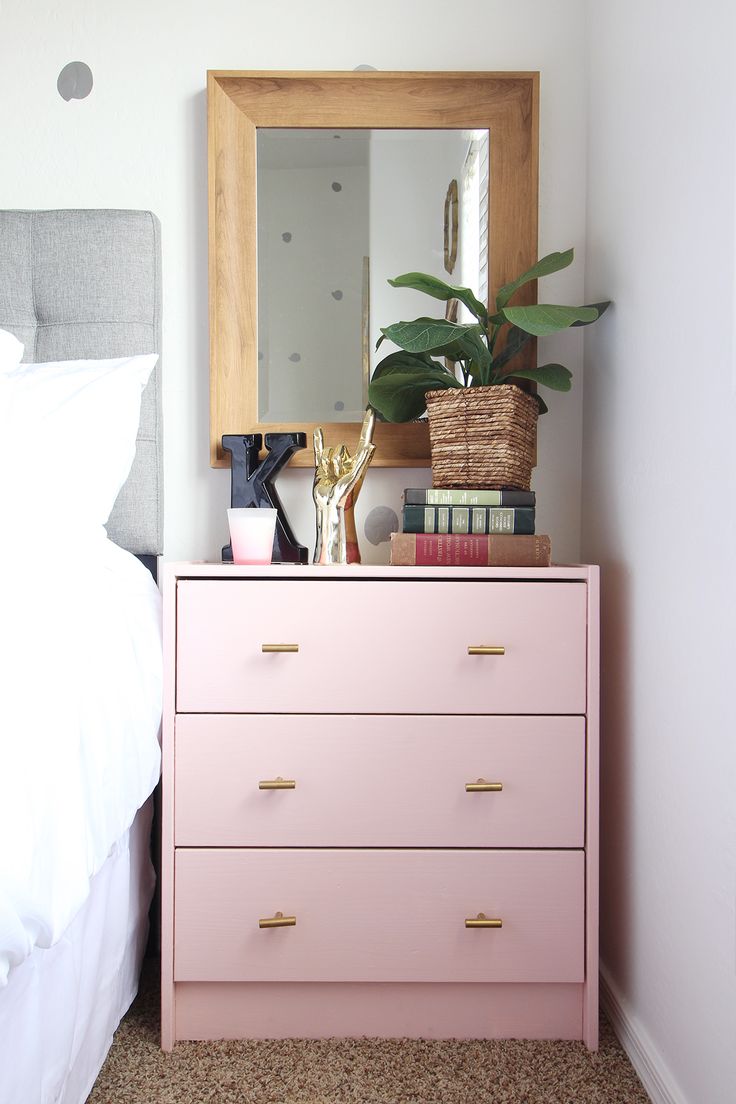 a pink dresser sitting next to a bed with a mirror on it's side