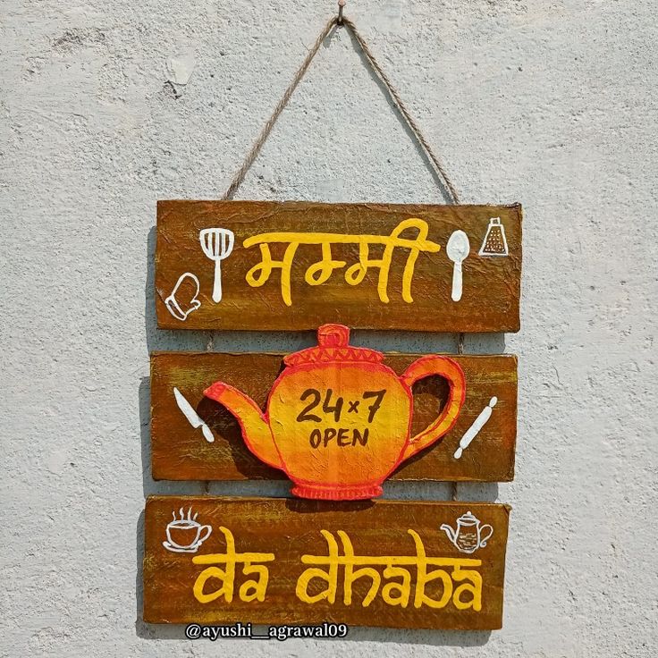 a wooden sign hanging on the side of a building with an orange teapot painted on it