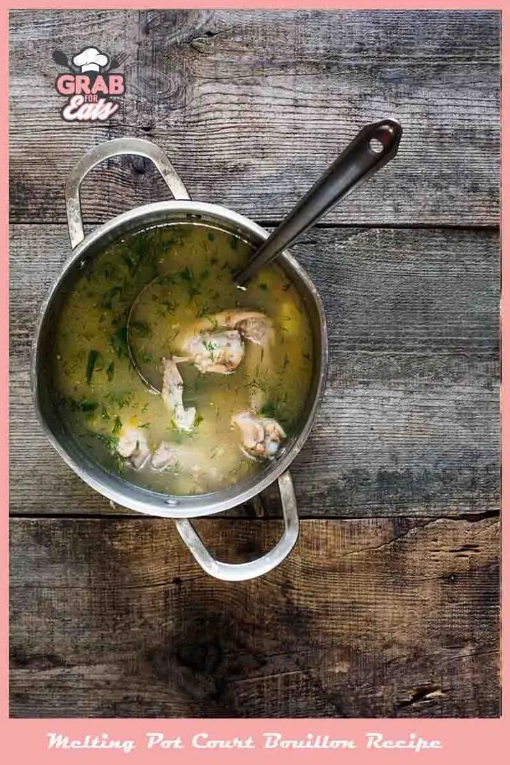 a pot filled with chicken and broth sitting on top of a wooden table next to a