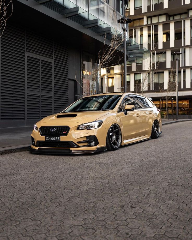 a gold subarunt is parked on the side of the road in front of a building