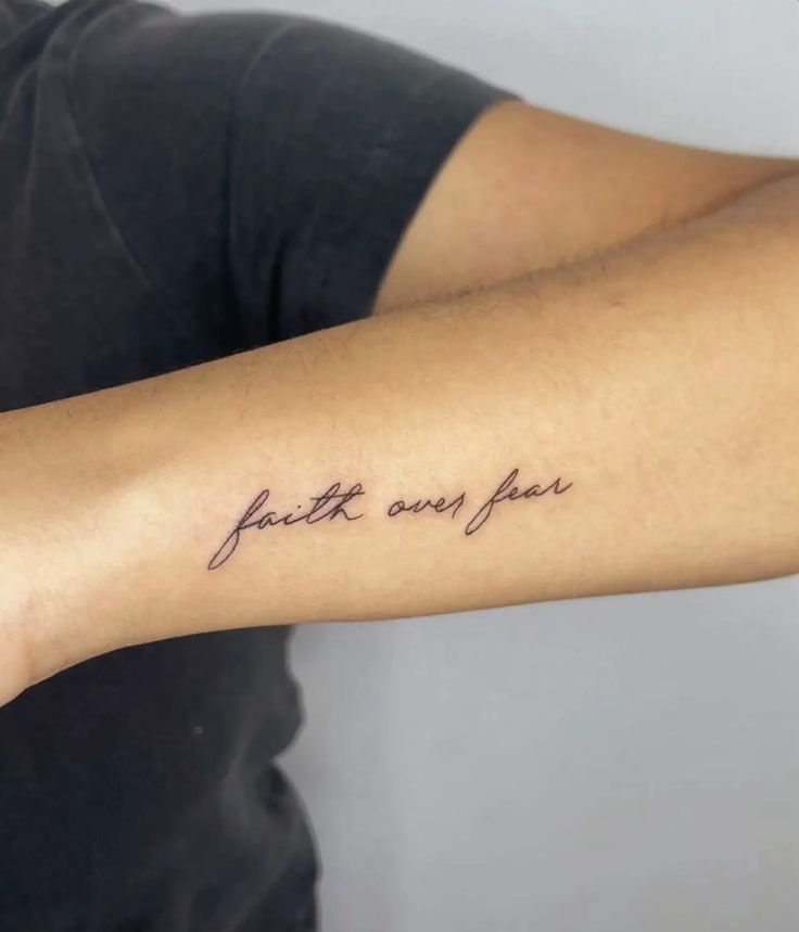 a person with a tattoo on their arm that says faith over fear in cursive writing