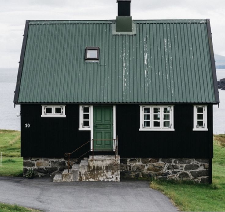 a black house with a green roof next to the ocean