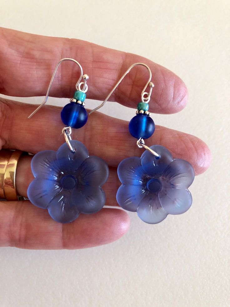 "Beautiful light sapphire blue or royal blue sea glass flowers are the feature of these pretty dangle earrings. Large 1\" sea glass flower is accented with contrasting shades of royal blue, teal and aqua blue sea glass rounds. Earrings are made of cultured tumbled sea glass and wire wrapped in German silver plated jeweler's wire. They hang from silver plated ear wires. Light sapphire blue earrings measure 2\" long and royal blue are 2 1/4\" long. Also available in Sterling silver. Listing is for Blue Sea Glass Nickel Free Earrings, Blue Sea Glass Nickel-free Earrings, Nickel-free Blue Sea Glass Earrings, Blue Flower Charm Drop Earrings, Blue Sea Glass Dangle Jewelry, Handmade Blue Sea Glass Earrings, Blue Flower-shaped Jewelry For The Beach, Blue Czech Glass Beach Jewelry, Blue Flower Shaped Earrings For Summer