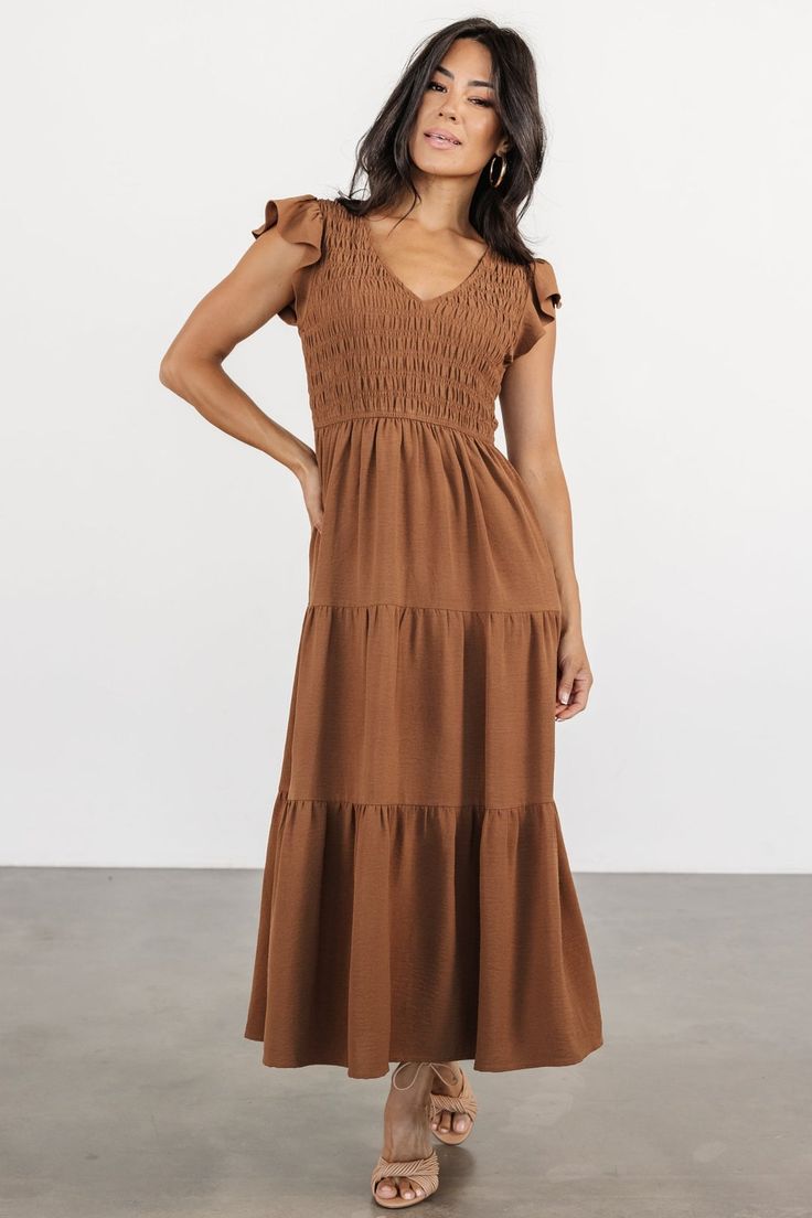 Introducing The Brandie, your new go-to choice for casual weekend brunch. With its warm medium brown hue, V-neckline, and cap-length flutter sleeves, this dress offers a relaxed yet stylish option, featuring a fully smocked bodice, natural waist, and midi-length skirt with three tiers for effortless charm. Spring Brown Midi Dress With Smocked Bodice, Brown Smocked Back Dress For Brunch, Brown Short Sleeve Dress With Smocked Bodice, Brown Ruffled Maxi Dress, Brown Dress With Smocked Bodice And Short Sleeves, Brown Dresses With Smocked Back For Brunch, Brown Dress With Smocked Back For Brunch, Brown V-neck Dress With Ruffle Hem, Brown Smocked Bodice Dress For Brunch