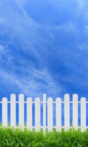 a white picket fence sitting in the middle of a lush green field with blue sky