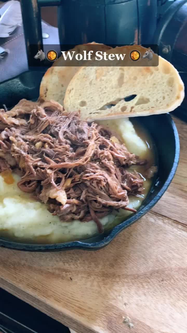 a bowl filled with meat and potatoes on top of a wooden table