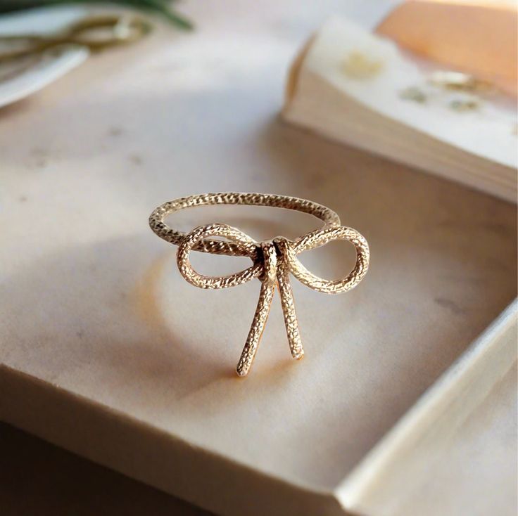 Sparkle Bow Ring - Available in Gold Filled or Sterling Silver Adorn your finger with the whimsy of the Sparkle Bow Ring. Available in gold filled for warmth and luster or in sterling silver for its bright and timeless elegance, this ring is the epitome of playful sophistication. The intricate bow is a classic symbol of celebration and individuality, with each handcrafted loop and twist catching the light, creating a dazzling display. Measuring delicately in size, it offers a charming statement that’s as versatile as it is delightful. With this ring, expect to carry a spark of joy and a dash of fancy with you wherever you go. Specifications: • Materials: Choose from Gold Filled or Sterling Silver• Design: Handcrafted bow with a textured finish• Size: Made to order in your ring size, bow me Handmade Elegant 14k Gold Stackable Rings, Elegant Handmade Yellow Gold Stackable Rings, Elegant Handmade 14k Gold Stackable Rings, Heirloom 14k Gold Midi Rings For Gift, Heirloom 14k Gold Midi Rings As Gift, Rose Gold Brass Wedding Ring, Delicate Adjustable Gold Stackable Rings, Adjustable Jewelry With Ring Detail For Gift, Gold Tiny Midi Rings Fine Jewelry