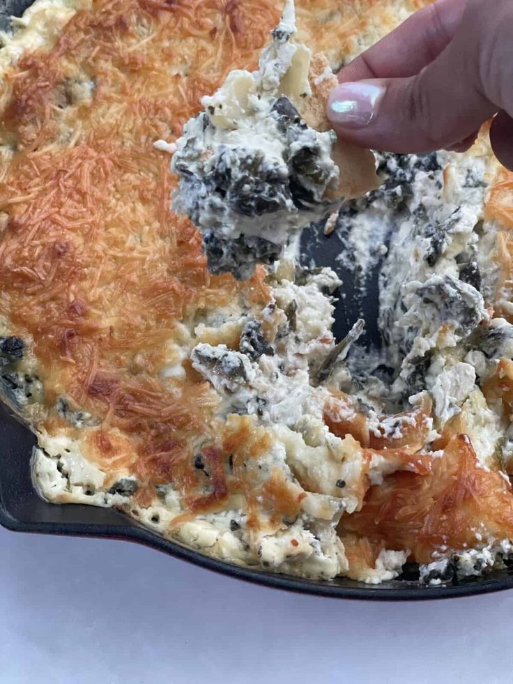 a person dipping something into a skillet filled with cheese and other toppings on it