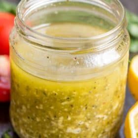 a jar filled with pesto sauce next to sliced lemons and tomatoes