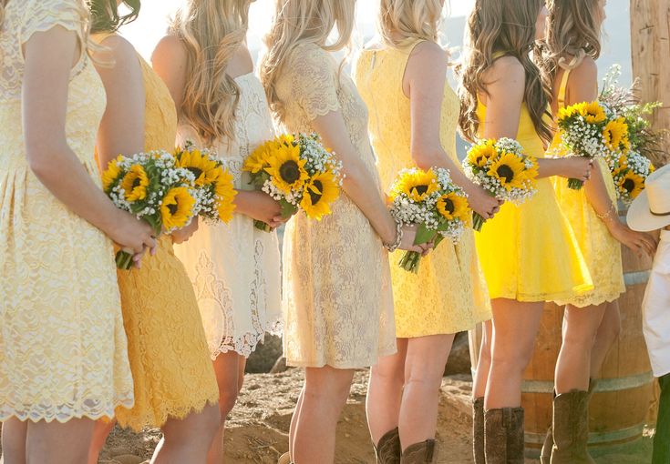 a group of women standing next to each other wearing yellow dresses and holding sunflowers