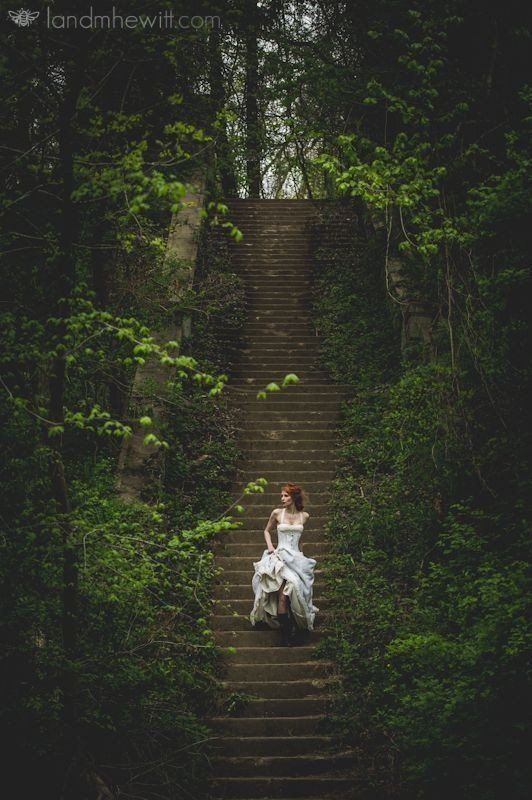 a woman in a white dress is sitting on some steps with trees and bushes behind her