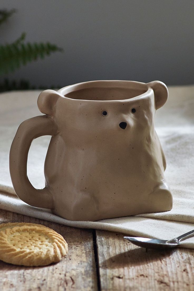 a ceramic bear mug sitting on top of a wooden table next to a cracker