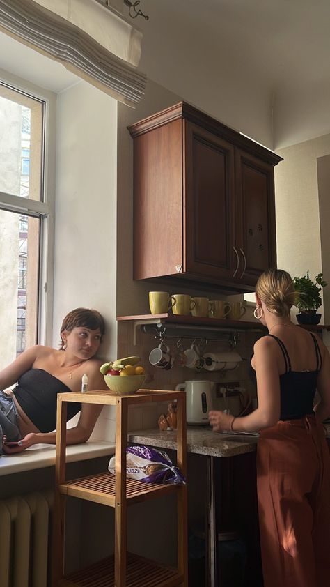 two women are in the kitchen looking out the window at the other woman on the counter