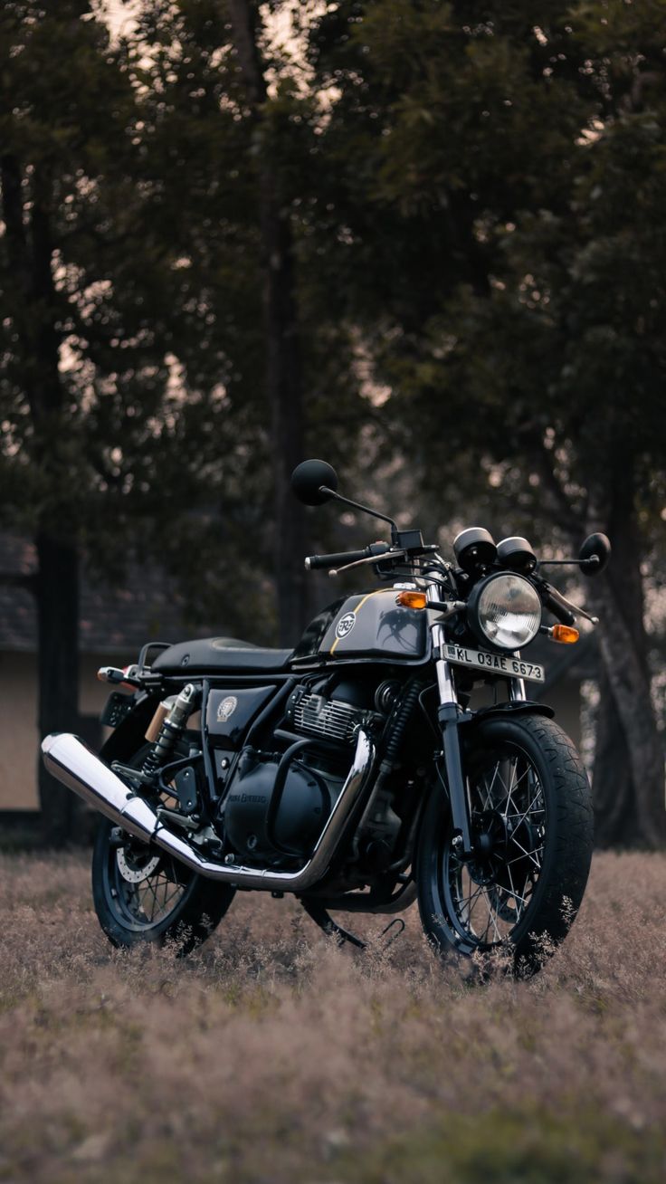 a motorcycle parked in the middle of a field with trees in the backgroud