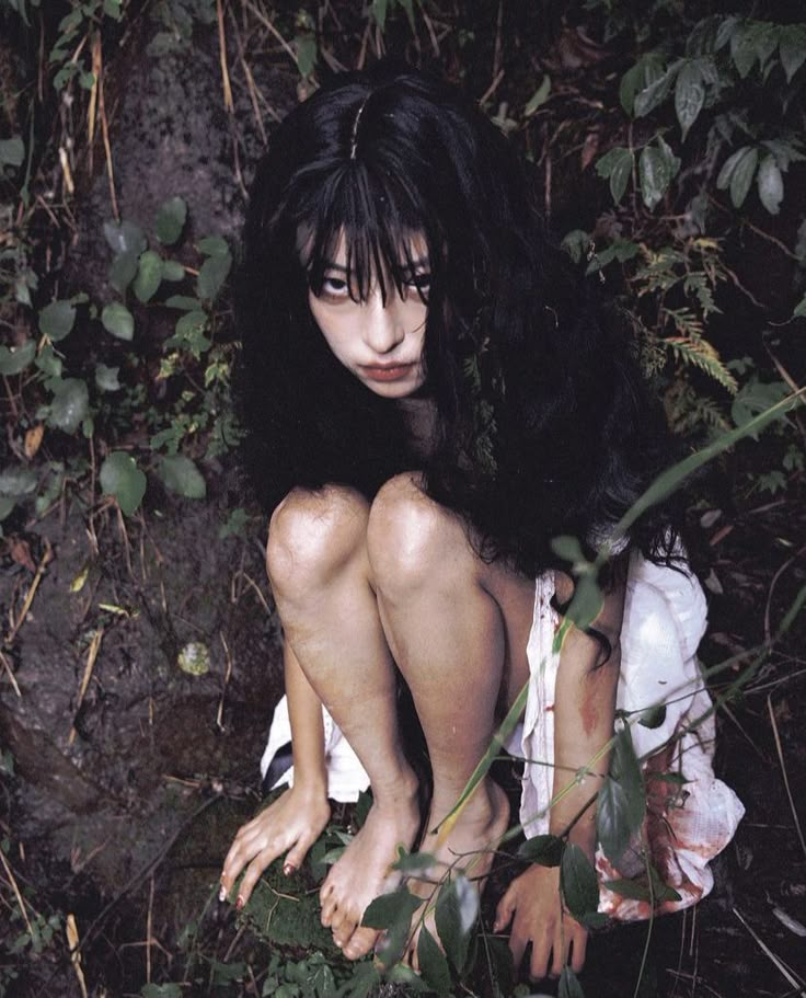 a woman sitting on the ground surrounded by plants