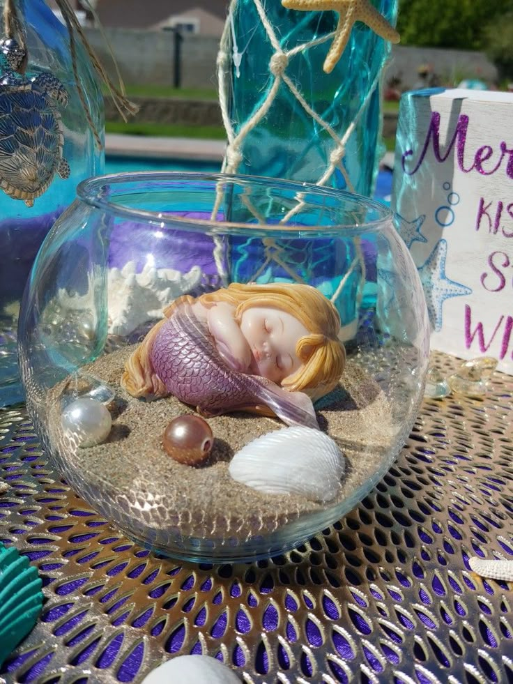 a glass bowl filled with sand and shells sitting on top of a table next to a sign