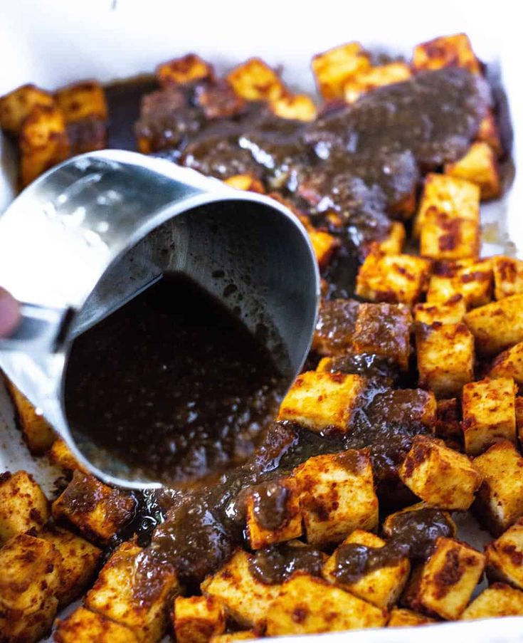 someone pouring sauce over tofu cubes in a white dish with brown gravy