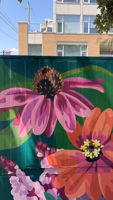 a large flower painted on the side of a green fence with buildings in the background