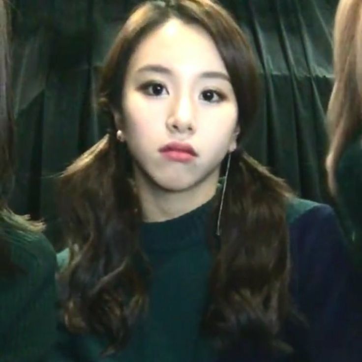 a woman with long brown hair is looking at the camera while wearing green sweater and earrings