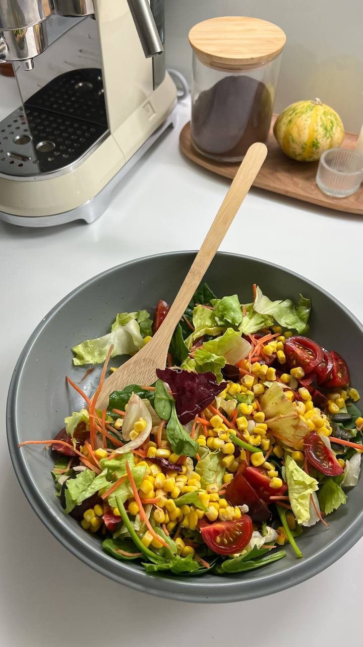 a salad is in a bowl with a wooden spoon on the table next to an espresso machine