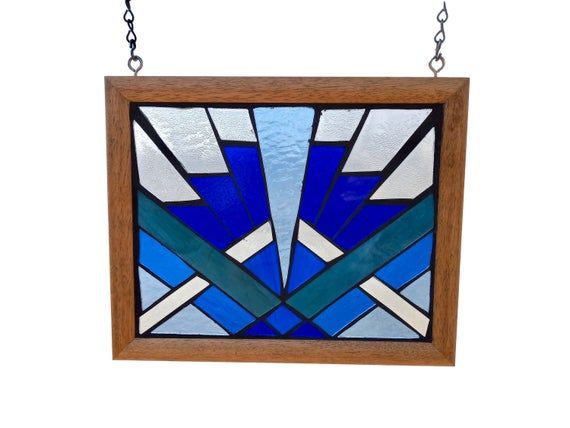 a blue and white stained glass window hanging from a metal chain on a white wall