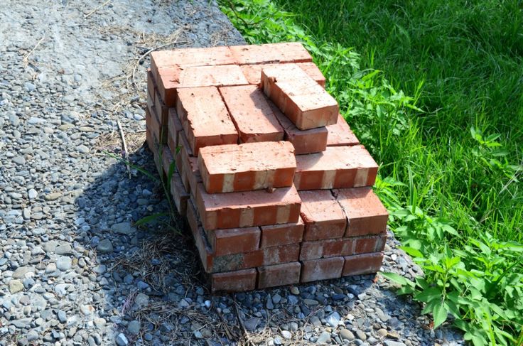 a pile of red bricks sitting on top of a gravel covered ground next to green grass