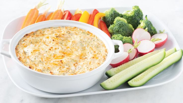 a bowl of dip surrounded by vegetables on a white platter with carrots, celery and radishes