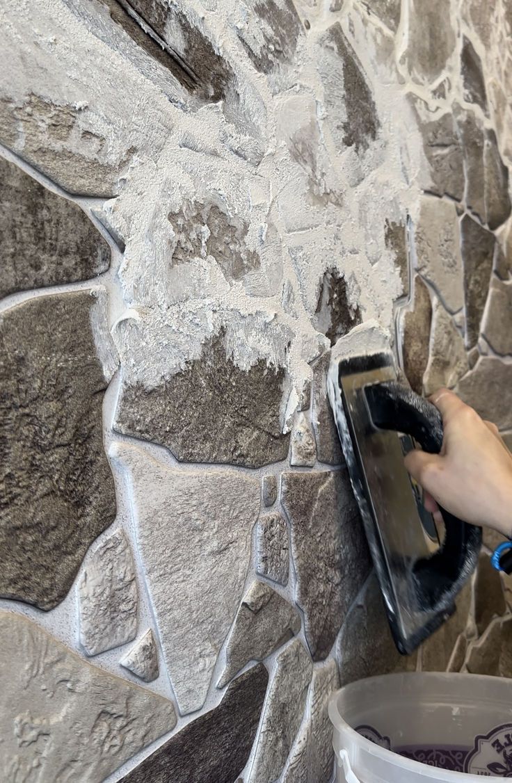 a person using a mop to clean a stone wall with a bucket on it